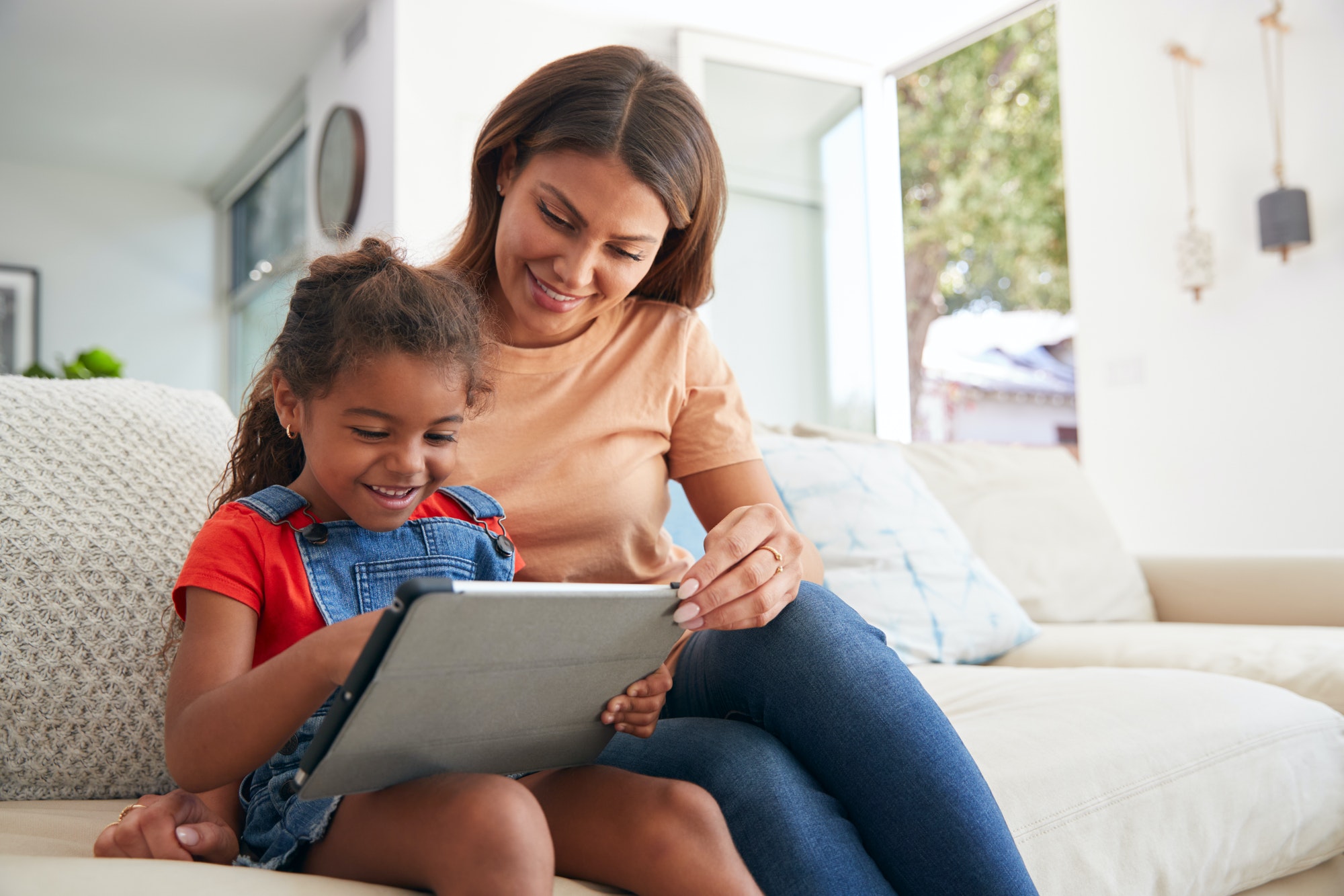 Hispanic Mother Helping Daughter To Home School And Do Homework With Digital Tablet