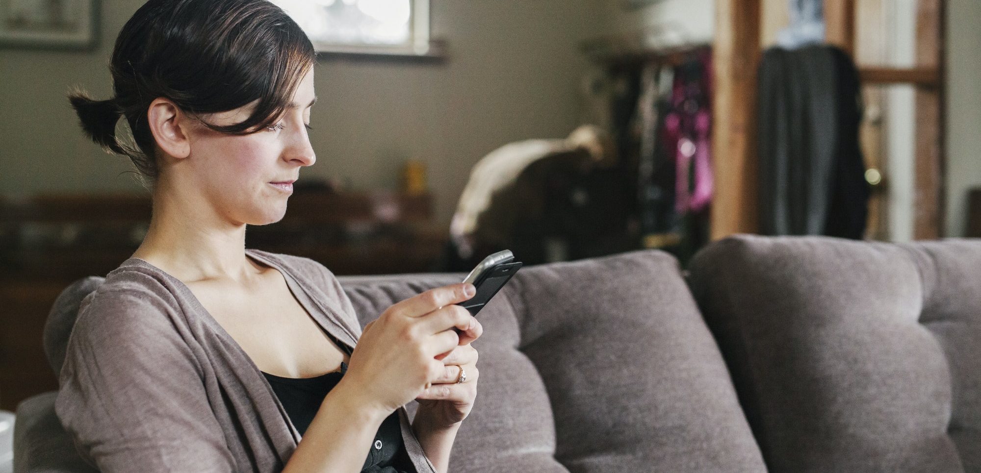 A woman on the sofa using her smart phone to text.